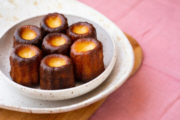 A plate of french pastries, Canelés de BordeauxCanelés de Bordeaux on a white plate and pink tablecloth from above