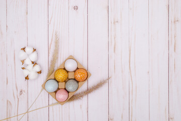 colorful eggs on white wooden background with the dry grass. Natural decor for Easter. 