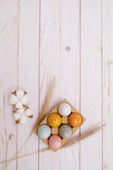 colorful eggs on white wooden background with the dry grass. Natural decor for Easter. 