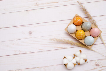 colorful eggs on white wooden background with the dry grass. Natural decor for Easter. 