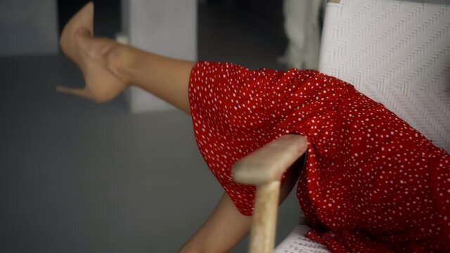 European girl with a red dress sitting across a white chair and shaking her legs