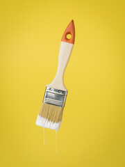 Paint brush with dripping white paint on a yellow background.