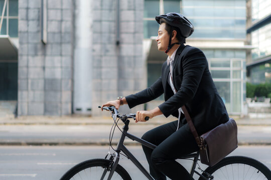 Asian businessman in a suit is riding a bicycle on the city streets for his morning commute to work. Eco Transportation Concept..