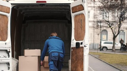 Delivery service. Man carrying boxes, parcels and putting them into white van. Urban background.