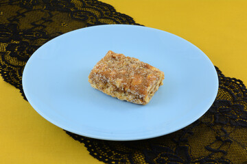 Brazilian pe de moca or peanut brittle toffee on blue snack plate on black lace table runner on yellow ocher tablecloth