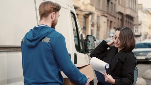 Delivery Service. Courier Delivering Box To Woman. Happy girl putting signature in clipboard to receive package.