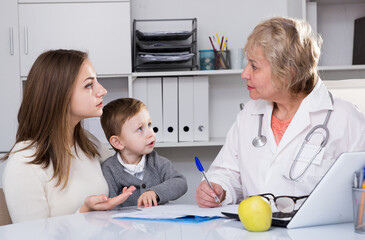 Adult female doctor is examining kid in clinic.