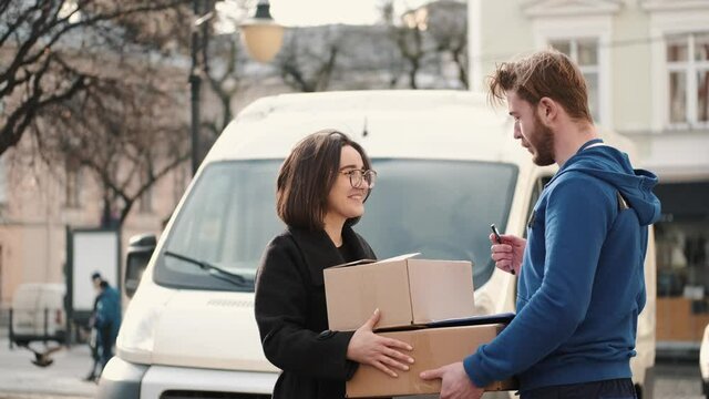Delivery Service. Courier Delivering Box To Woman. Happy girl putting signature in clipboard to receive package.