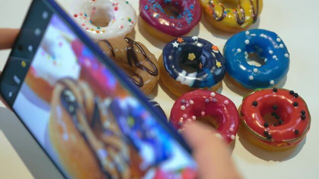 A photo is taken on a smartphone. Delicious donuts of different colors lie on a white table. Donuts are covered with confectionery glaze and sprinkles. Close-up. Photo concept for social networks.