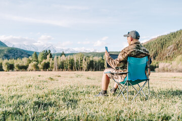 one person using smartphone and laptop sitting in the chair on the meadow