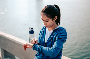 Young asian woman check the pulse via a smartwatch after jogging a morning workout in the city. A city that lives healthy in the capital. Exercise, fitness, jogging, running, lifestyle, healthy.