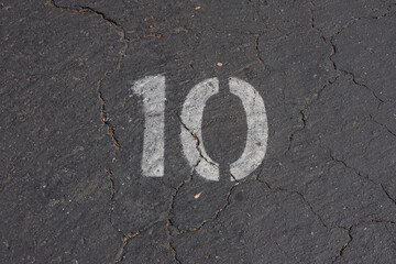 A parking space marked on the asphalt with the white paint stenciled number 10