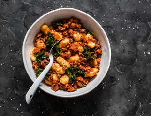 Gnocchi potatoes with turkey bolognese sauce and kale on a dark background, top view