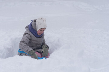 Fototapeta na wymiar The girl is digging the snow. The child plays with a lot of snow. A rosy child in the cold. Nice walk and play