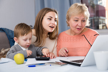 Fototapeta premium Aged woman is mastering technology near laptop with her daughter and grandson at home.