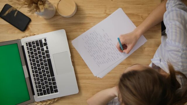 The girl writes down the main points from the conference. A laptop with a green screen. Top view. Remote work and training via the Internet. Make important notes on paper