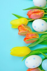 Fototapeta na wymiar Easter holiday.Orange and yellow bright tulips and variegated decorative easter eggs on a blue background.copy space.Spring Religious Holiday Symbol. Easter festive background