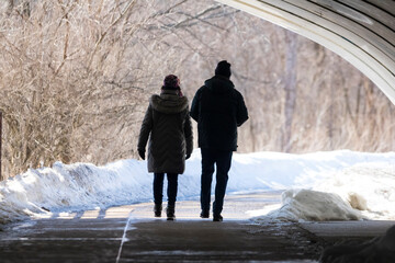 A couple walking together outdoors on a sunny day under a bridge.