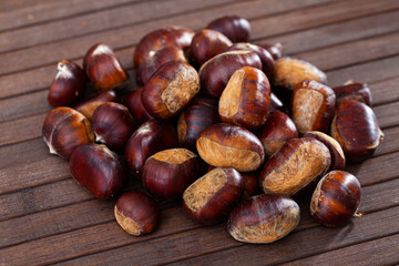 Obraz premium Closeup of pile of peeled edible chestnuts on wooden table ready for roasting..