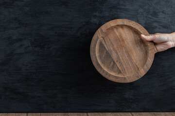 Holding a wooden platter in the hand on black background