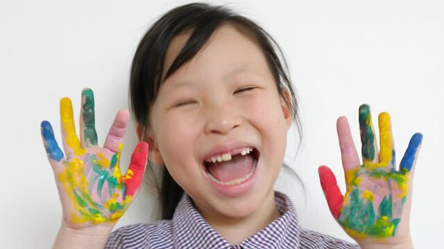 Little asian girl laughing at camera and show her palms in paints. 