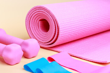 Sports mat and pink dumbbells on brown background close-up.