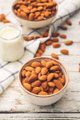 Bowls of almonds and jar of milk on light wooden background