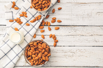 Bowls of almonds and jar of milk on light wooden background