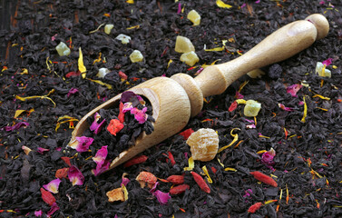 black blended tea with flower petals and dried fruit on a wooden scoop.