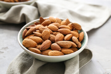 Plate with tasty almonds on grey background