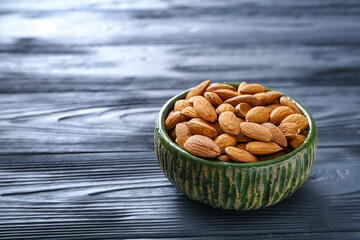 Bowl with tasty almonds on wooden background