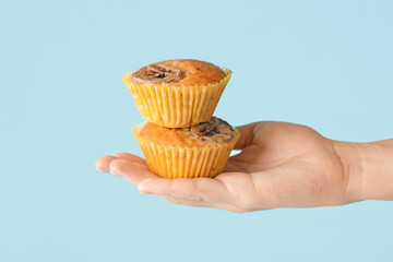 Female hand with tasty banana muffins on color background