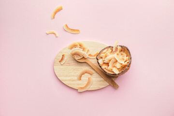 Spoon with tasty coconut chips on color background