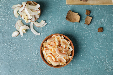 Bowl with tasty coconut chips on color background