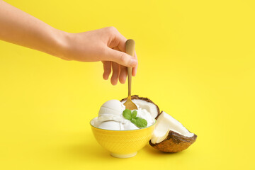 Female hand and bowl with tasty coconut ice cream on color background