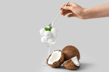 Female hand with tasty coconut ice cream on light background