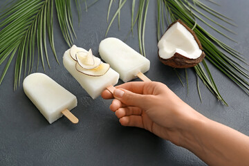 Female hand with tasty coconut ice cream on dark background
