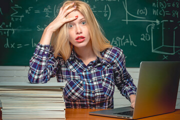 Desperate woman student on classroom background. Young teacher sitting at table and writing on notebook.