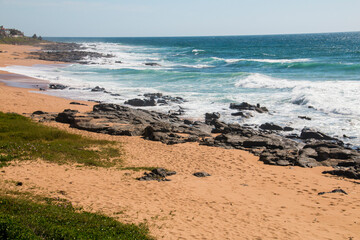 Dune Covered with Vegetation and Black Rocks in Sea