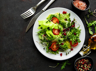 Fresh green mixed  salad bowl with tomatoes and microgreens  on black concrete background. Healthy food, top view.