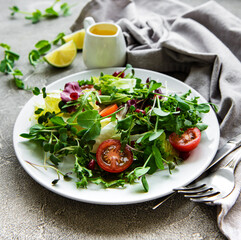Fresh green mixed  salad bowl with tomatoes and microgreens  on  concrete background. Healthy food, top view.