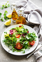 Fresh green mixed  salad bowl with tomatoes and microgreens  on  concrete background. Healthy food, top view.