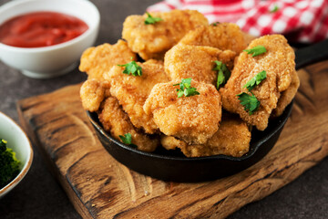 Homemade chicken nuggets with vegetables on a wooden board, close-up