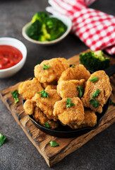 Homemade chicken nuggets with vegetables on a wooden board, close-up