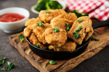 Homemade chicken nuggets with vegetables on a wooden board, close-up