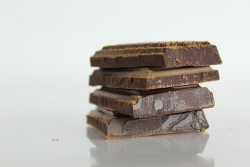 Dark bitter chocolate pieces stacked slide lies on a white background with a reflection with a place for text and copyspace