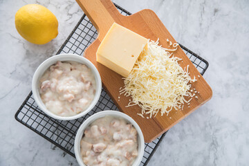 Typisches DDR Würzfleisch Ragout Fin mit geriebenen Gouda Käse in Auflaufform Schale und Zitrone auf Abkühlgitter und Marmor Hintergrund hell