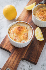 Typisches DDR Würzfleisch Ragout Fin mit geriebenen Gouda Käse überbacken in Auflaufform Schale und Zitrone auf Holzbrett und Marmor Hintergrund hell
