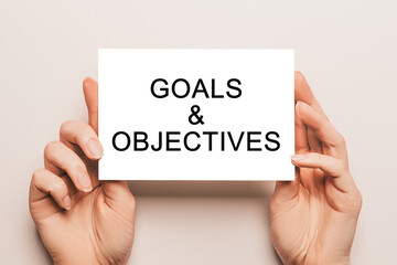 Female hands hold card paper with text Goals and Objectives on a yellow background. Business and finance concept