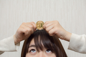 A young woman holds a bitcoin on her head.